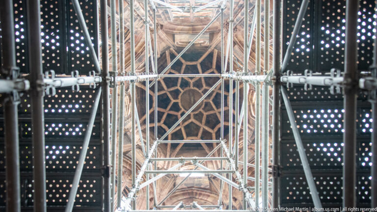 Dense metal scaffolding and perforated work platforms surround carved sandstone inside Strasbourg Cathedral’s tower structure.