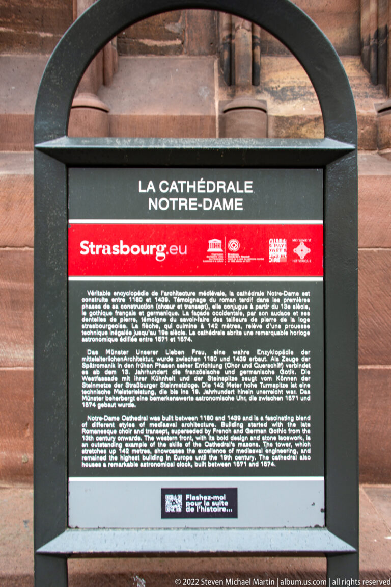 Black-framed visitor plaque reading “La Cathédrale Notre-Dame” and “Strasbourg.eu” mounted on pink sandstone.