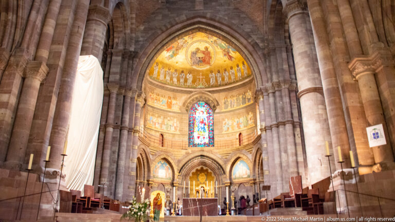 Stone arches frame Strasbourg Cathedral’s choir and apse with altar, stained glass, and a brightly decorated semi-dome.