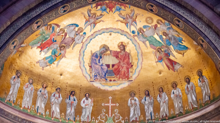 Painted and gilded celestial scene with Christ, the Virgin, angels, and standing saints above the cathedral astronomical clock.