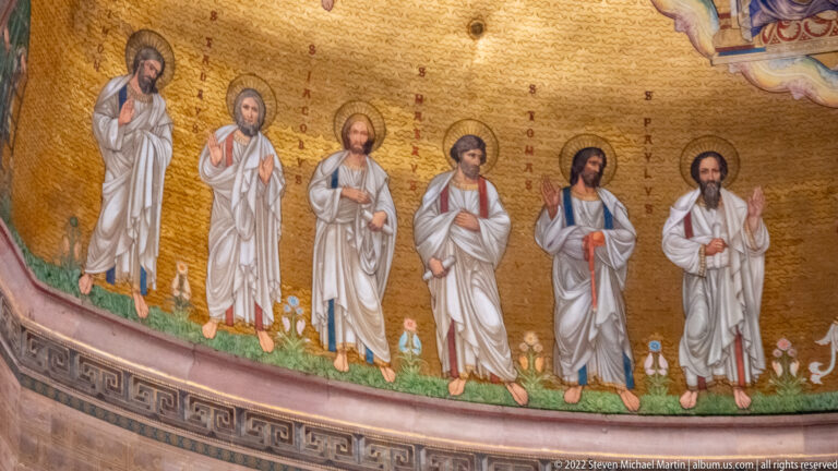 Six haloed robed saints stand in a row against a gold background above the astronomical clock.