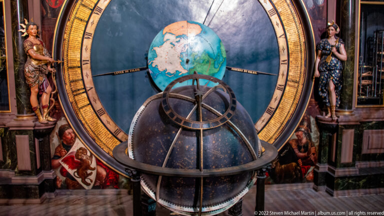 Terrestrial globe and nested metal rings stand before a large celestial dial in Strasbourg Cathedral.