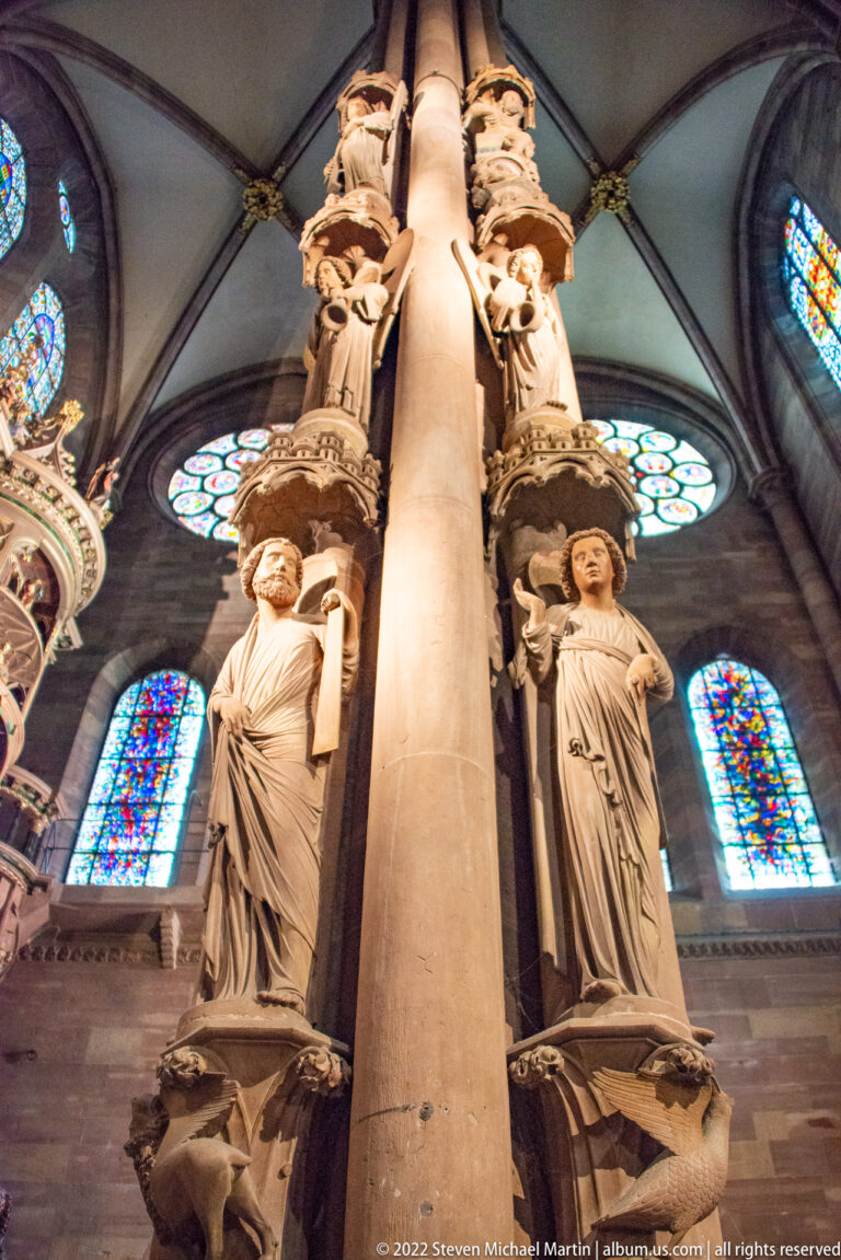 Carved figures of the Pillar of Angels rise around a stone pier with stained-glass windows behind.