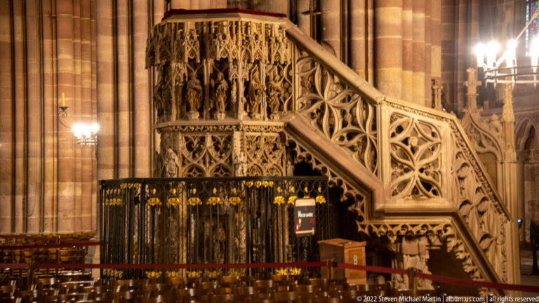 Carved Gothic stone pulpit with openwork stair balustrade and sculptural niches beside a cathedral pier.