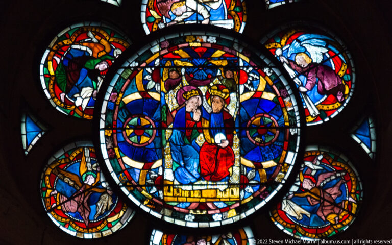 Circular stained-glass medallion with two haloed seated figures surrounded by smaller narrative roundels.