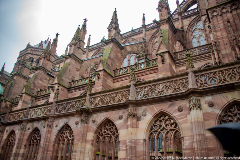 Oblique exterior view of Strasbourg Cathedral with sandstone buttresses, pinnacles, tracery, and pointed windows.