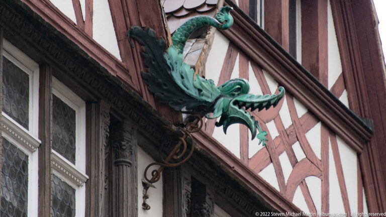 Green winged dragon hanging sign projects from an iron bracket on a red-and-white half-timbered building.