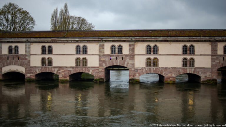 Long masonry Barrage Vauban crosses the river with multiple broad arches and rows of paired windows.