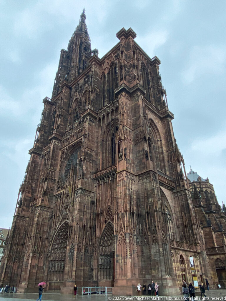 Low oblique view of Strasbourg Cathedral showing the west front, side elevation, buttresses, tracery, and tower.