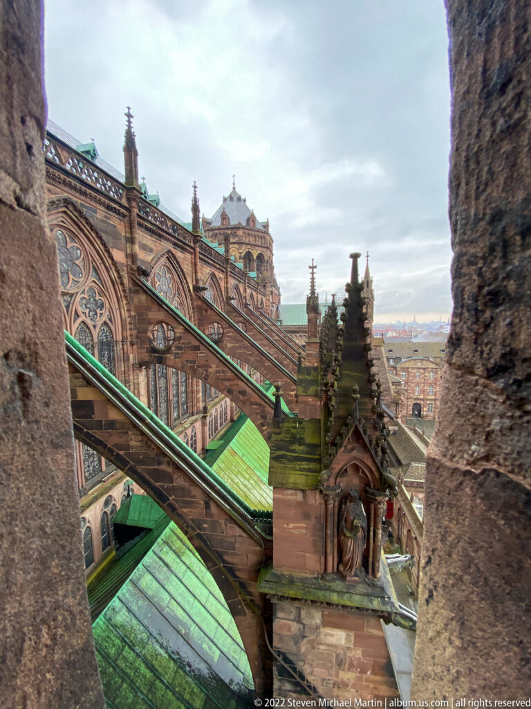 Flying buttresses, green copper roofs, and carved pinnacles seen from an upper level of Strasbourg Cathedral.