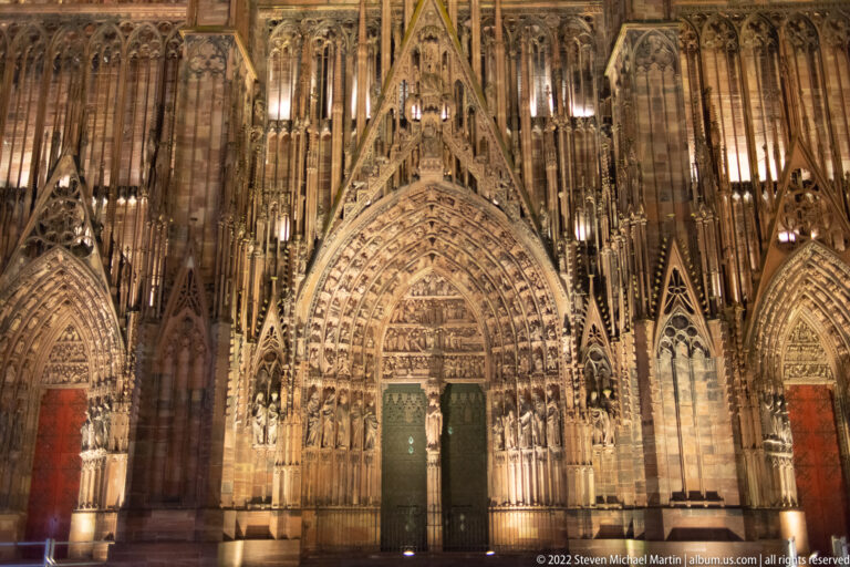 Illuminated central Gothic portal of Strasbourg Cathedral with dense sculpture, archivolts, and a pointed gable.