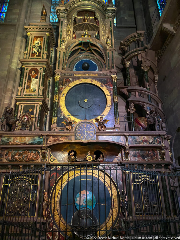 Strasbourg Cathedral astronomical clock with large blue-and-gold dial, terrestrial globe, painted panels, and iron railing.