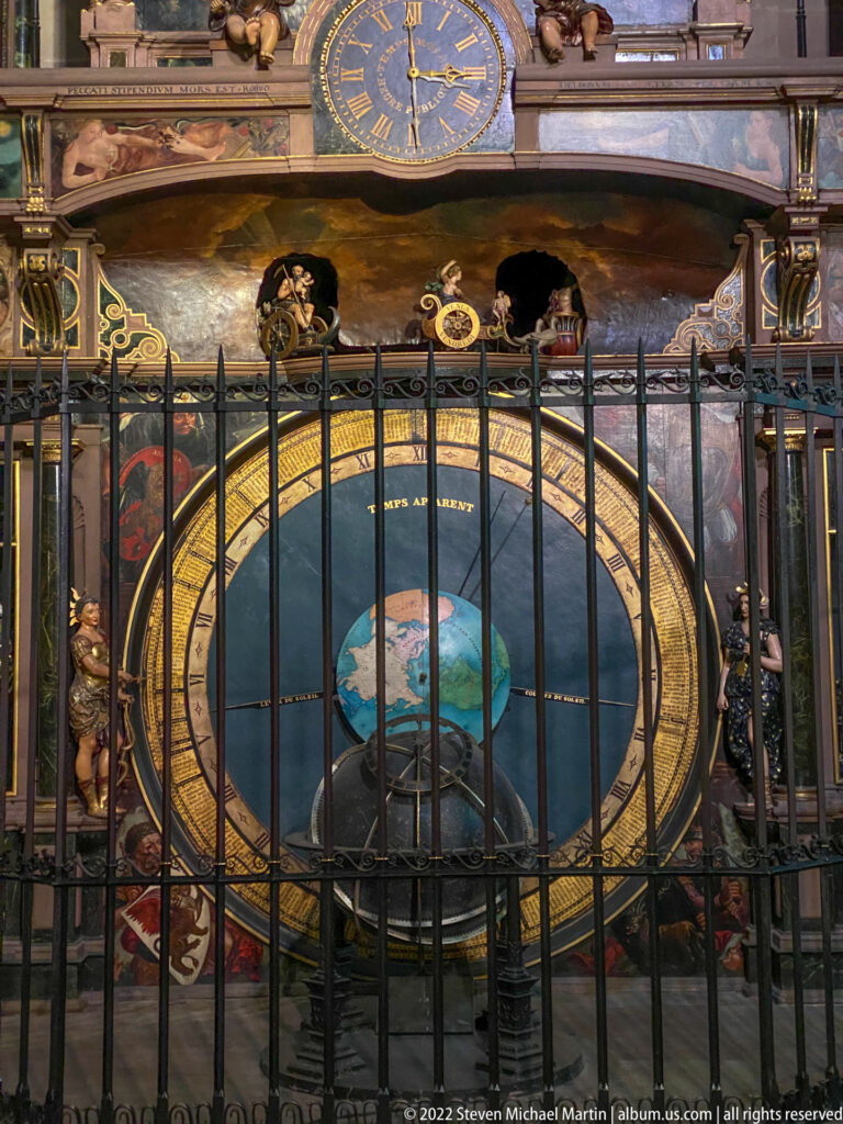 Close view of the astronomical clock's lower globe, gold-ringed display, small dials, painted figures, and iron barrier.