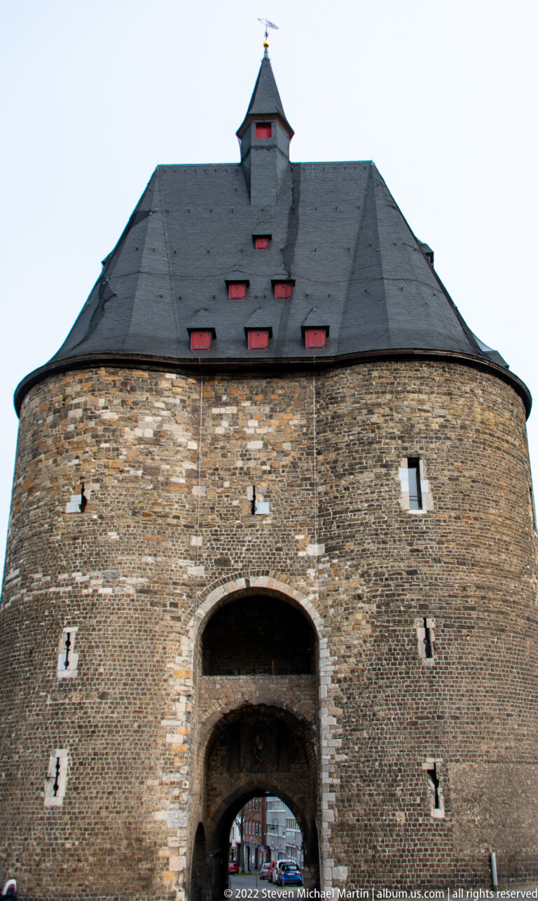 Medieval stone gatehouse with a steep slate roof, central arched passage, and small defensive openings.