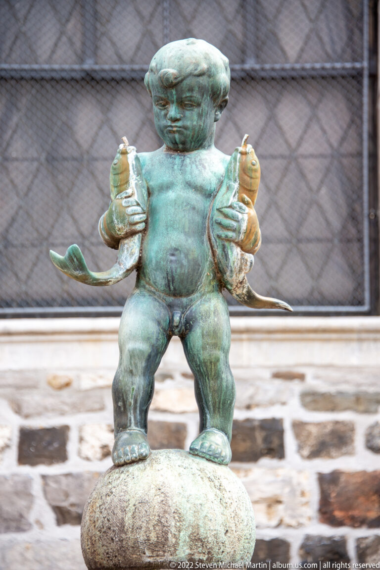Patinated bronze boy holding a fish in each hand on the Fischpüddelchen fountain in Aachen.