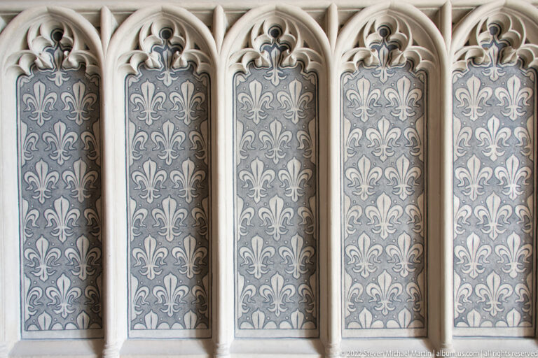 Vertical Gothic-style panels with cusped arches and repeated fleur-de-lis motifs on a dark patterned background.