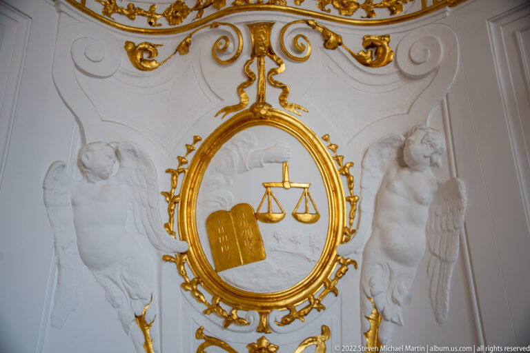 Two white stucco angels flank a gilded cartouche with tablets and a balance scale.