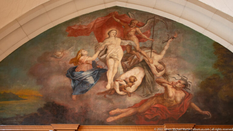 Curved mural with a pale central woman rising among winged and semi-nude figures beneath red and blue drapery.