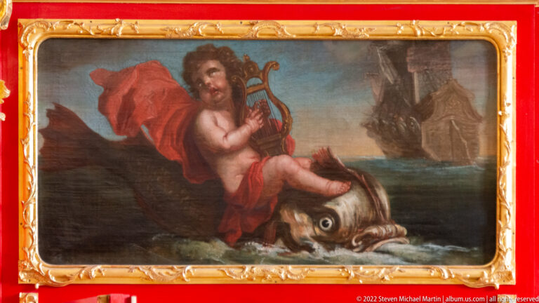 Painted male figure in red drapery playing a lyre above a large fish or sea creature.