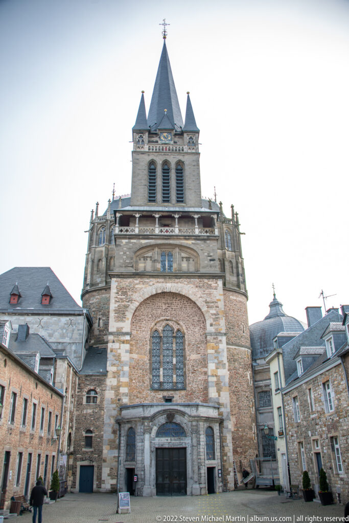 West façade of Aachen Cathedral with massive masonry tower, central spire, corner turrets, and entrance below.