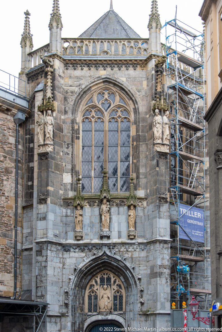 Stone Gothic church façade with large tracery window, saint statues, pinnacles, and scaffolding.