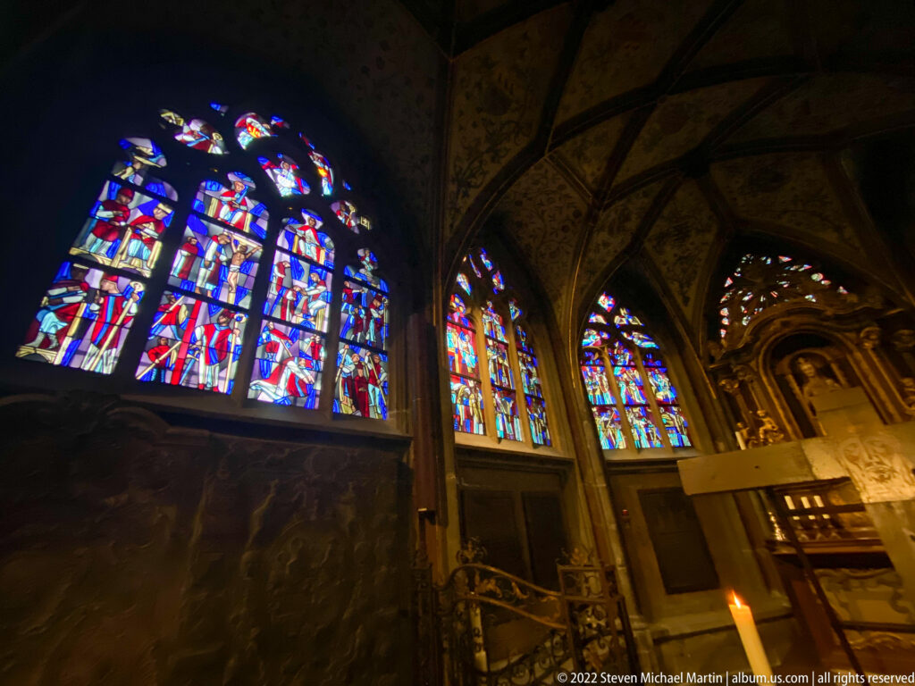 Bright red, blue, and white stained-glass windows glowing within the dark interior of Aachen Cathedral.