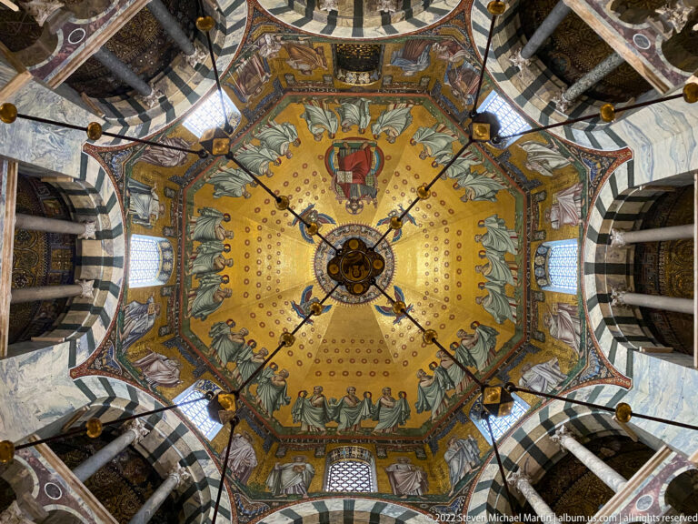 Upward view of Aachen Cathedral's golden Octagon mosaic with sacred figures arranged around the central chandelier suspension.