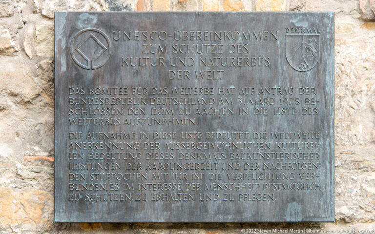 Bronze German-language UNESCO World Heritage plaque mounted on rough stone at Aachen Cathedral.