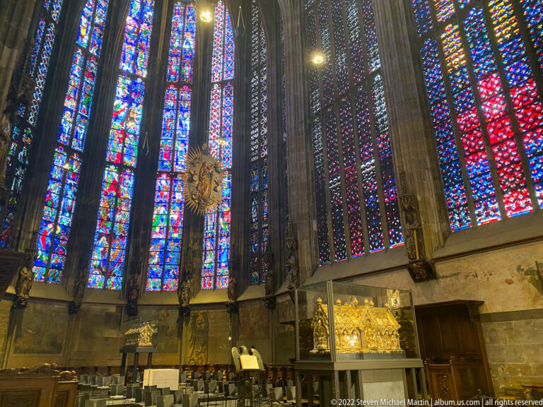 Tall stained-glass choir windows in Aachen Cathedral with a gilded shrine displayed at lower right.