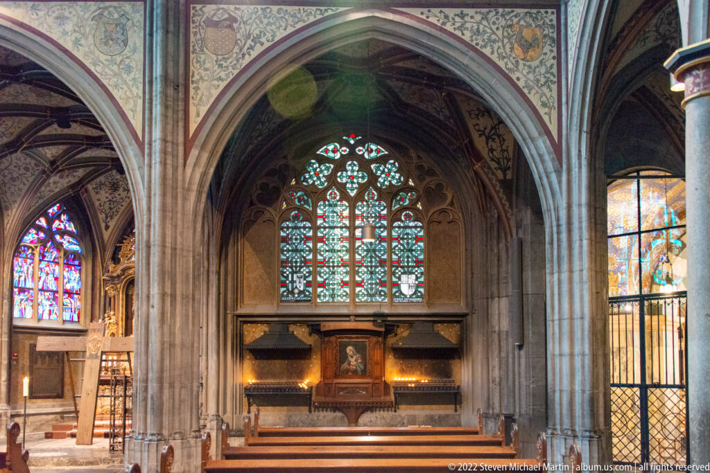 Gothic chapel in Aachen Cathedral with pointed arch, altar, stained-glass window, ribbed vaulting, and metal screen.