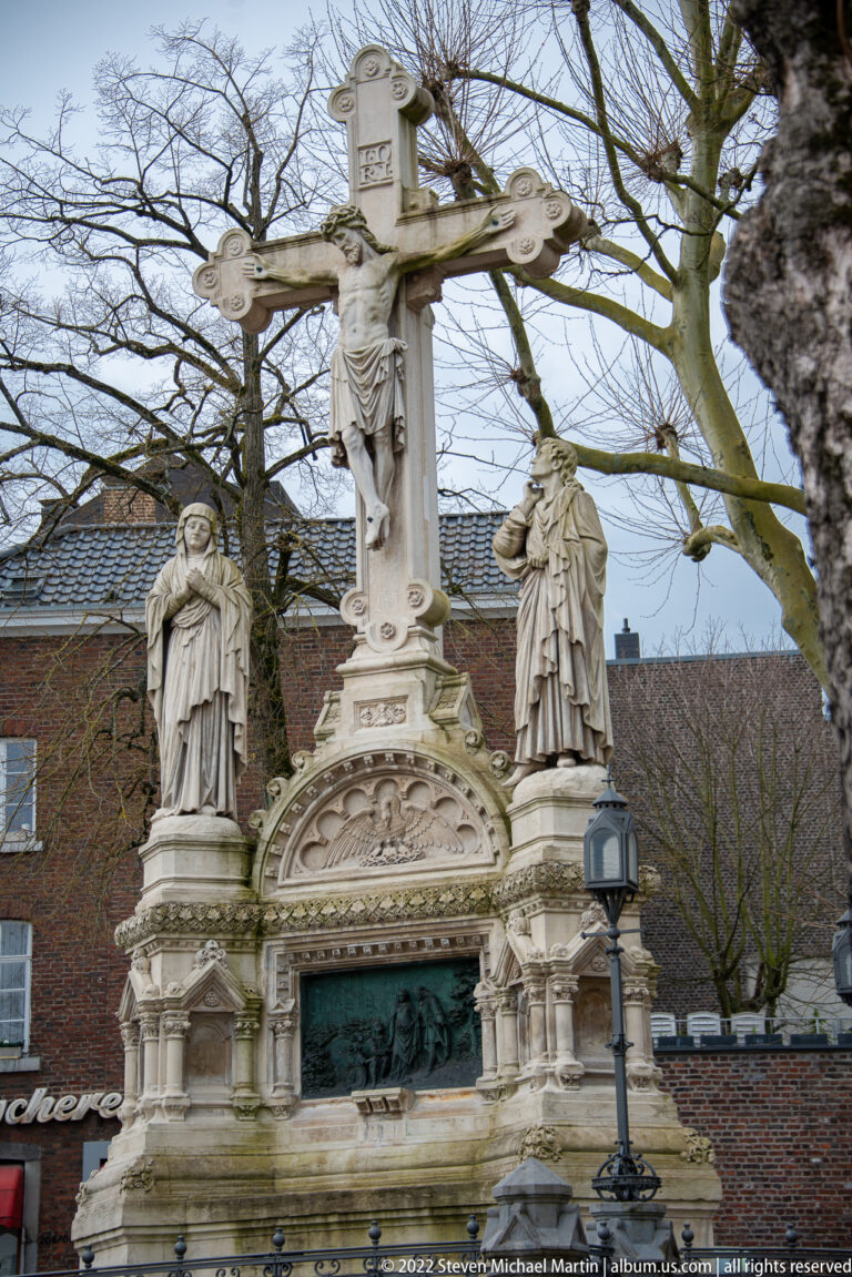 Stone Calvary monument with crucified Christ above an ornate base and two standing figures at the sides.