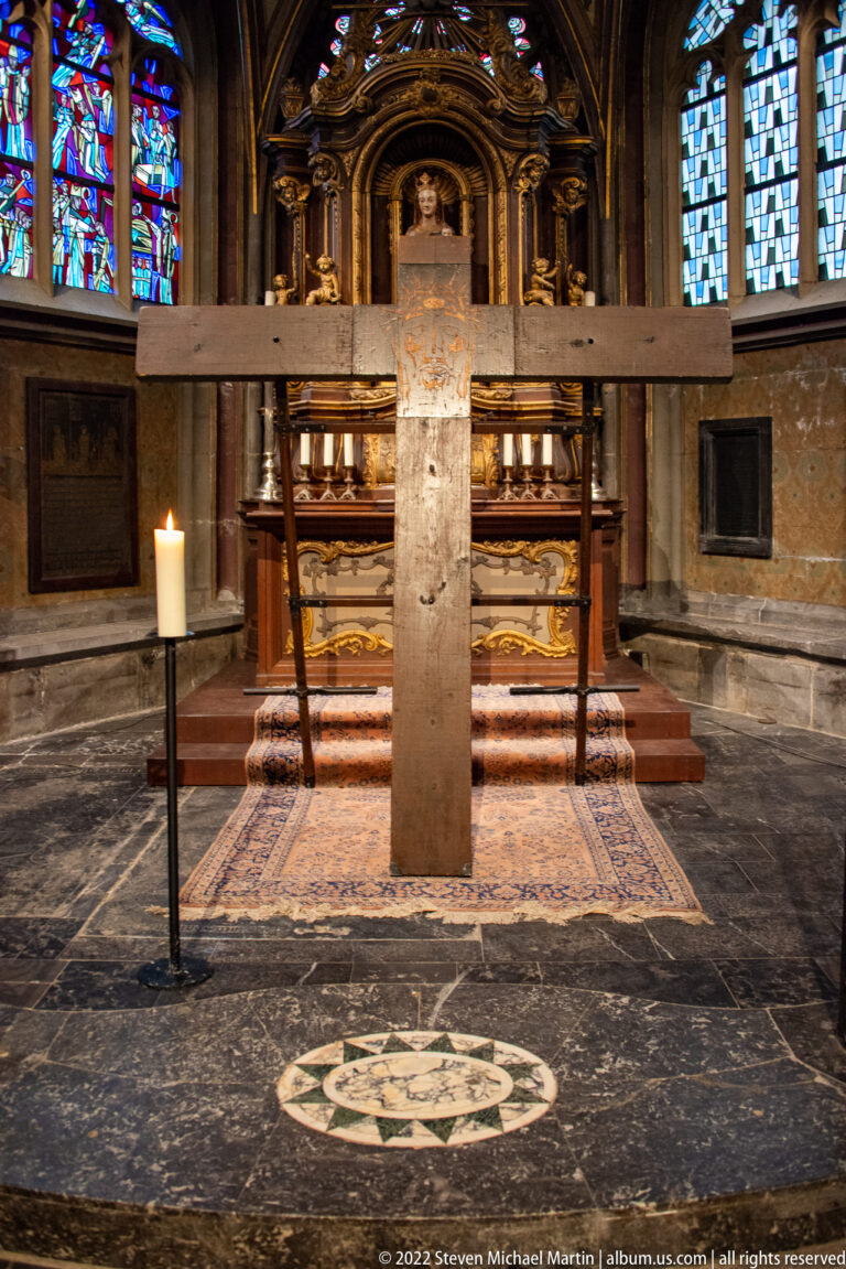 Stone marker before an altar behind a wooden rail, with candles and patterned floor paving inside Aachen Cathedral.
