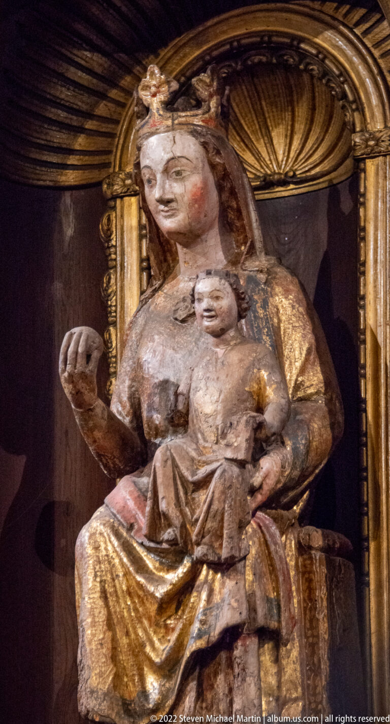 Weathered polychrome Madonna and Child seated beneath a gilded carved canopy.