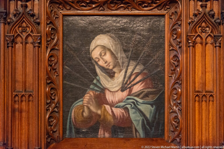 Devotional painting of the sorrowful Virgin with clasped hands in a carved Gothic-style wooden frame.