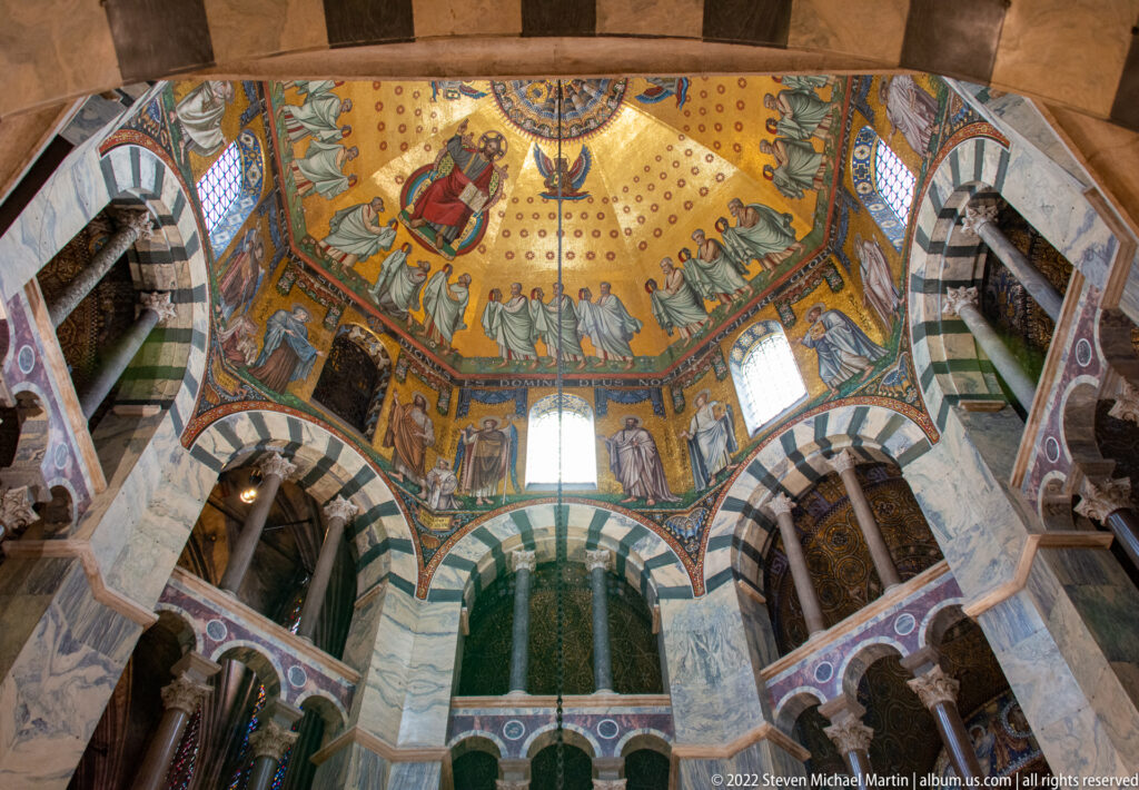 Upward view into Aachen Cathedral’s Octagon, with gold dome mosaic above striped arches, galleries, and marble surfaces.