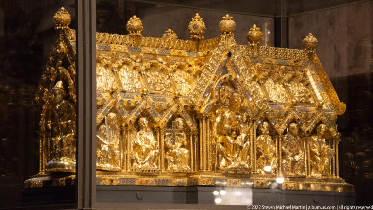 Gilded Gothic reliquary shrine with pointed gables, finials, and standing figures displayed behind glass in Aachen Cathedral.