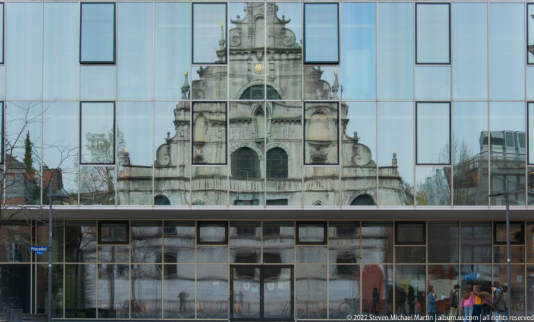 Historic gabled façade reflected across a grid of windows on a modern glass-fronted building.