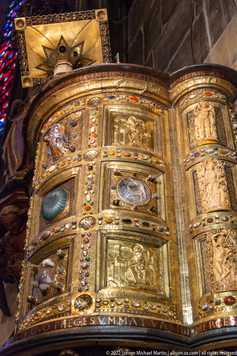 Curved gilded liturgical object covered with relief plaques, colored gems, beaded borders, and inscriptions.