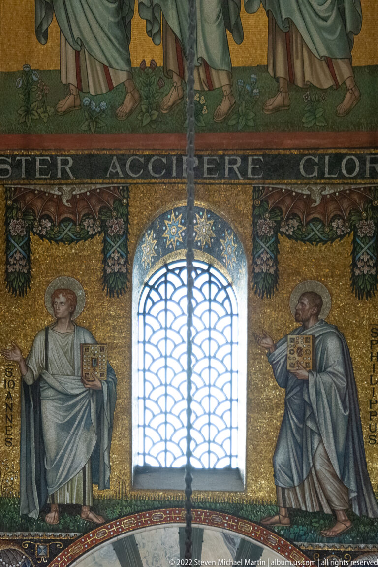 Two haloed mosaic saints holding books stand on either side of a tall central window.
