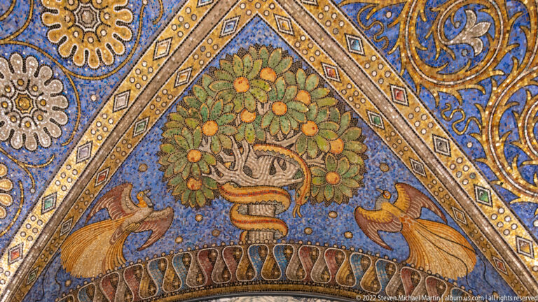 Fruit-bearing tree in a triangular blue mosaic panel, flanked symmetrically by two birds and gold ornament.