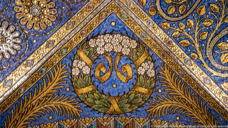 Interlaced blue monogram inside a white floral wreath on a deep blue mosaic ground with gold ornament.