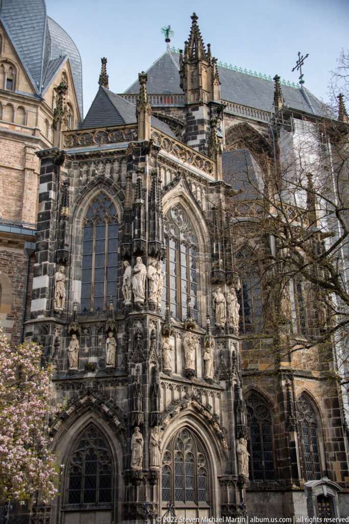 Gothic choir exterior of Aachen Cathedral with tall traceried windows, buttresses, pinnacles, and stone figures.