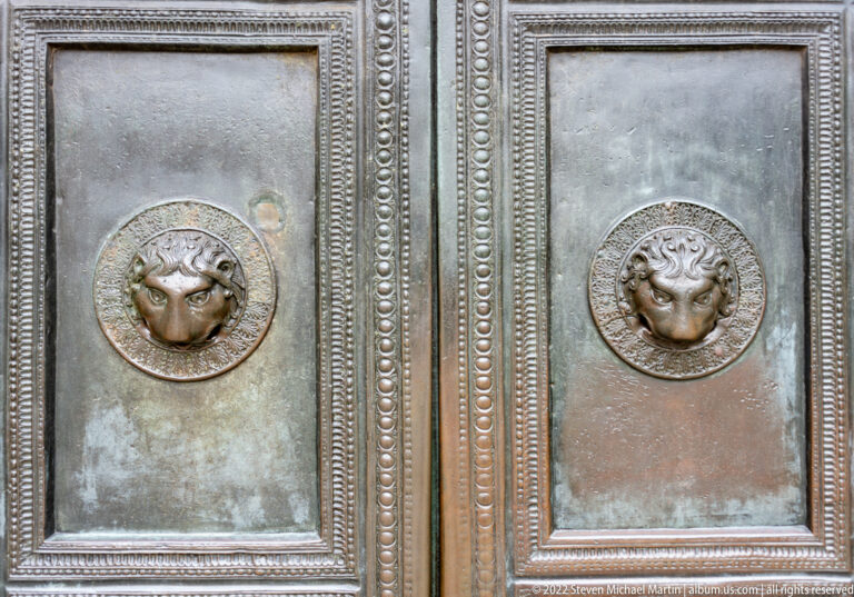 Paired bronze door panels with lion-head ring handles, beaded borders, and green-brown patina.