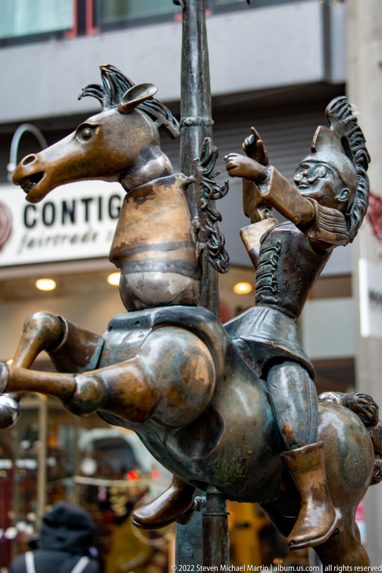 Close view of two playful bronze figures, one astride an animal-like form and another leaning backward with raised arms.