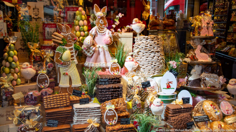 Confectionery shop window crowded with stacked biscuits, decorated sweets, small figures, and product labels.