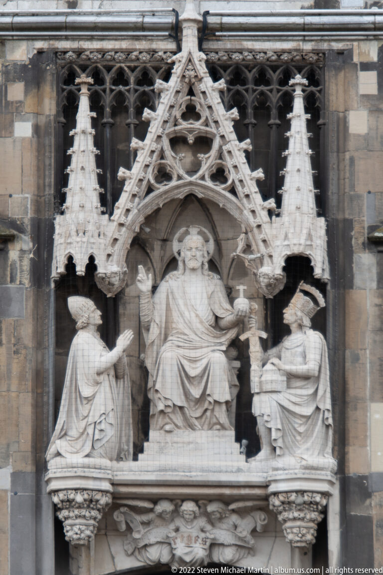 Stone relief of an enthroned ruler with two flanking figures beneath a pointed Gothic canopy.