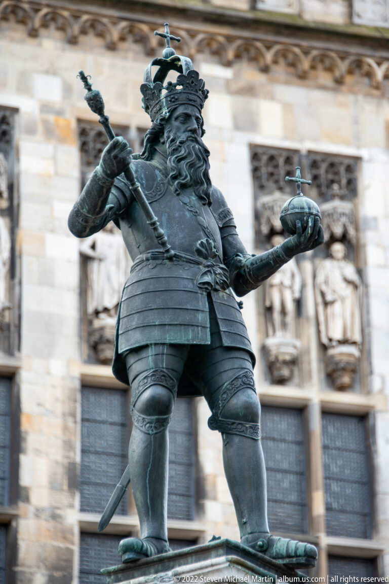 Bronze crowned ruler in armor holding an orb, with a staff or weapon at his side.