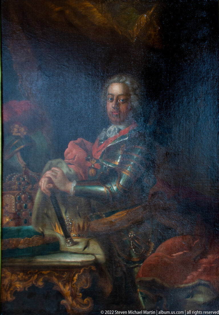 Dark oil portrait of a seated man in armor, with his face and hands emerging from a shadowed interior.