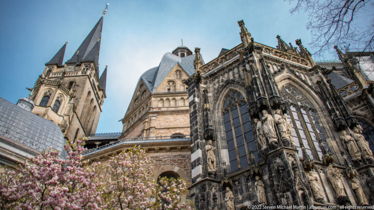 Low-angle exterior view of Aachen Cathedral combining the towered westwork, central volumes, and Gothic choir.