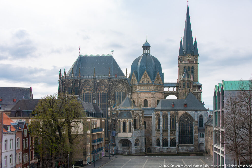 Elevated view of Aachen Cathedral with Gothic choir, octagonal dome, tall tower, and surrounding historic-center buildings.